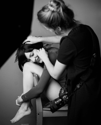 Mara Saiz colocando con las manos el pelo de una clienta que sonríe, en blanco y negro, cámara al hombro